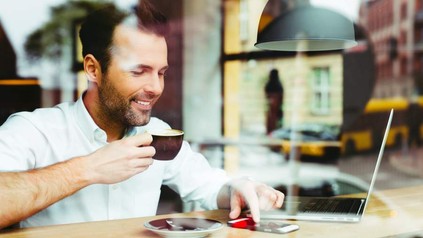 Mann trinkt Kaffee und sieht auf sein Smartphone