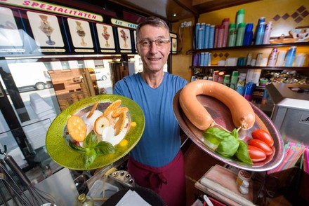 Ein Mitarbeiter präsentiert in der einen Hand Eis und in der anderen eine Wurst