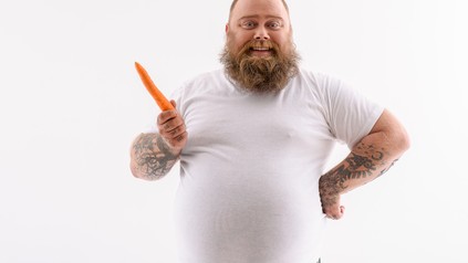 Dicker bärtiger Mann mit Karotte in der Hand