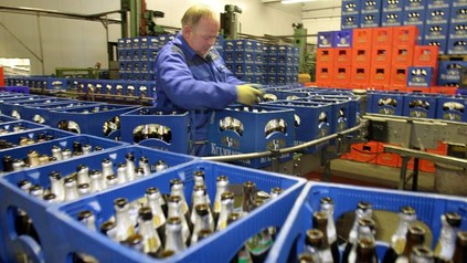 Ein Mitarbeiter steht inmitten hunderter Bierkästen mit Leergut und stapelt diese auf ein Laufband