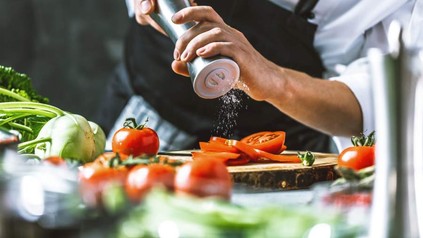 Ein Koch salzt eine aufgeschnittene Tomate mit einer Salzmühle