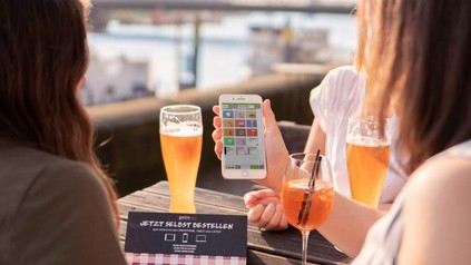 Junge Frauen an einem Tisch mit Bier und Sprizz, die auf ein Smartphone blicken