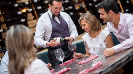 Wirt schenkt Gästen Rotwein ein