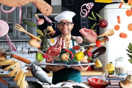 Ein Koch mit einem Kochbuch aus dem alle möglichen Zutaten fliegen