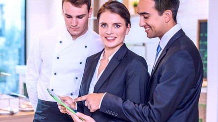 Eine Frau und zwei Männer, Hotel-Angestellte, die in ein Tablet schauen