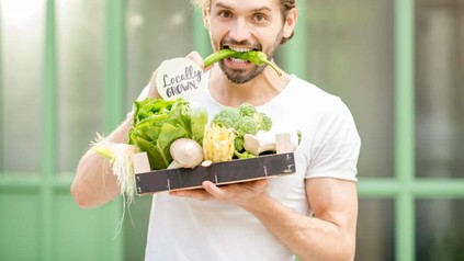 Ein junger Mann mit diversem Gemüse in der Hand beißt in eine Pepperoni auf der Locally Grown steht