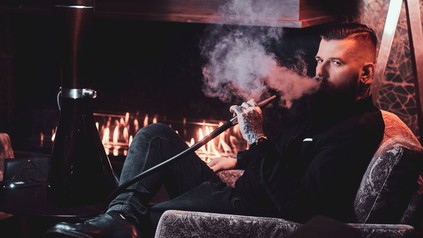 Bärtiger Mann beim Rauchen einer Shisha, im Hintergrund ein Kaminfeuer