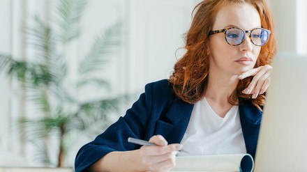 Rothaarige Frau sitzt mit Stift vor einem Laptop