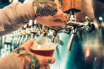 Zwei tattoowierte Hände zapfen ein Bier