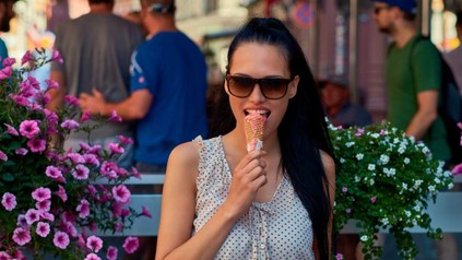 Eine hübsche Frau isst draußen lächelnd ein Eis