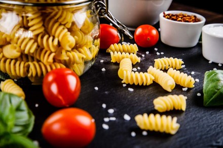 Ein Tisch auf dem sich Nudeln, Tomaten und Basilikum tummeln