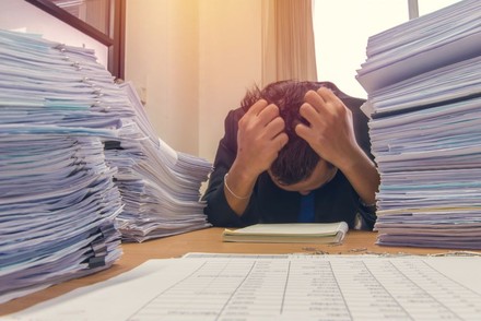 Mann verzweifelt vor riesigem Stapel