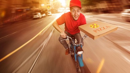 Pizzalieferant auf Mofa mit Pizzaschachtel in der Hand