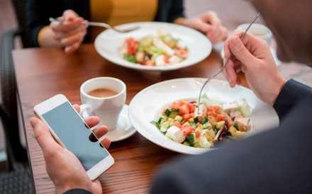 Zwei Personen essen gemeinsam während eine der beiden das Smartphone in der Hand hält