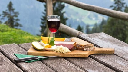 Eine deftige Brotzeit angerichtet auf einem Holzbrett vor einem Bergpanorama