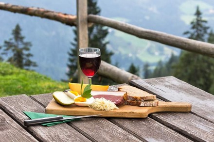 Eine deftige Brotzeit angerichtet auf einem Holzbrett vor einem Bergpanorama