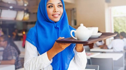 Eine Servicekraft mit Kopftuch serviert Tee