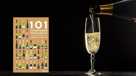 Ein Nachschlagewerk über Sekte und Champagner, daneben eine Sektglas, in das jemand Schaumwein einschenkt