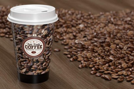 Ein Kaffeebecher mit der Aufschrift Fair Trade Coffee vor einem Menge Kaffeebohnen