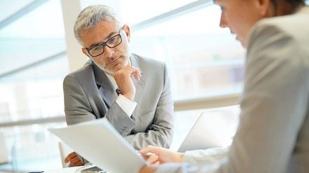 Ein älterer Herr im Anzug lässt sich von einer Frau etwas erklären bzw. sich beraten