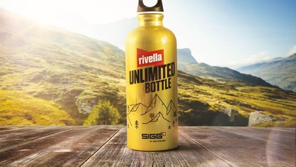 Die goldene Rivella Unlimited Bottle vor einem Bergpanorama