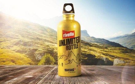 Die goldene Rivella Unlimited Bottle vor einem Bergpanorama
