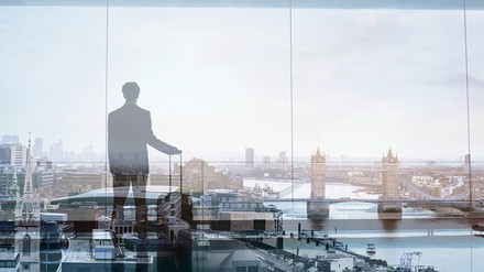 Abstrakte Darstellung eines Geschäftsreisenden vor spiegelnder Fensterfront mit der Silhouette von London mit der Tower Bridge