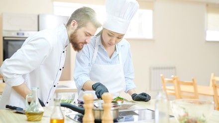Azubi schaut Köchin beim Anrichten über die Schulter