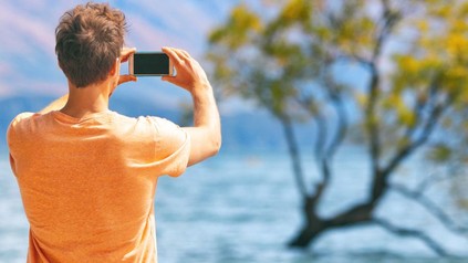 Ein Mann fotografiert mit seinem Smartphone einen Baum