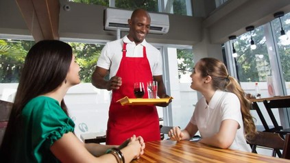 Ein Mann schwarzer Hautfarbe bedient fröhlich zwei Gäste im Restaurant