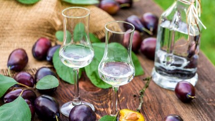 Gläser mit Schnaps und Pflaumen im Hintergrund