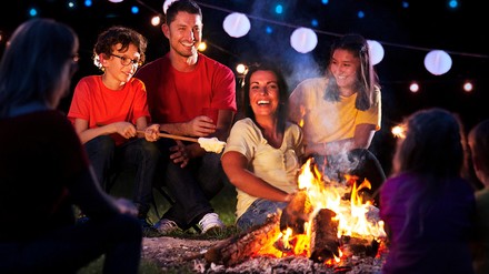 Vierköpfige Familie sitzt mit Stockbrot am Lagerfeuer