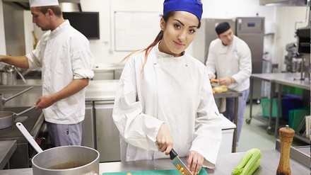 Junge Frau, Kochauszubildende schneidet Gemüse und blickt in die Kamera