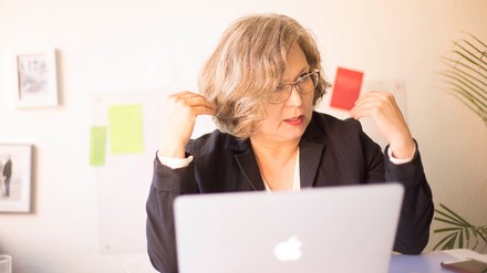 Eine Frau sitzt vor einem Apple-Laptop und spricht