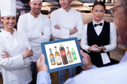 Ein Gastronom mit einem Tablet in der Hand auf dem diverse Getränke zu sehen sind