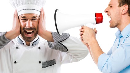 Ein Mann im Hemd schreit einen Koch mit einem Megafon an