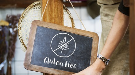 Nahaufnahme einer Frau mit Schürze, die eine Tafel mit der Aufschrift „Gluten Free“ aufhängt; glutenfreie Ernährung
