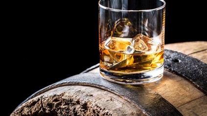 Ein Whiskyglas mit Eiswürfeln auf einem alten Holzfass