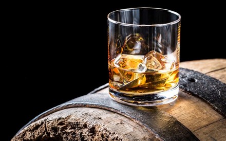 Ein Whiskyglas mit Eiswürfeln auf einem alten Holzfass