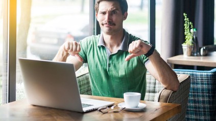 Mann sitzt vor Laptop und macht Daumen-runter-Geste.