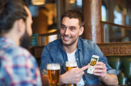 Ein junger Mann, der an einem Tisch sitzt und seine Rechnung mit dem Smartphone und der barforce-App begleicht.