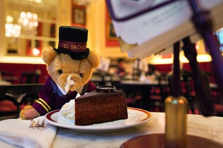 Bär in Pagengewand vor Kuchen auf Tisch