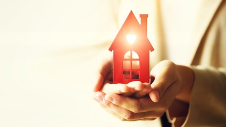 Zwei Hände halten ein rotes Hausmodell