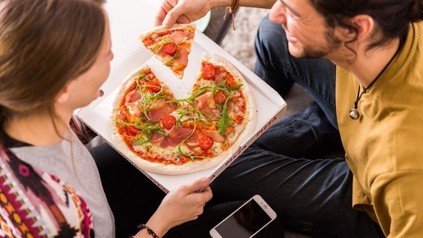 Ein junges Pärchen isst eine Pizza neben der ein Smartphone liegt
