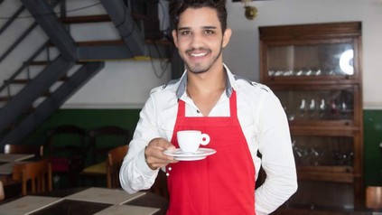 Ein lächelnder syrischer Kellner mit einer Tasse Kaffee in der Hand