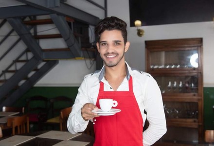 Ein lächelnder syrischer Kellner mit einer Tasse Kaffee in der Hand