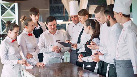 Auszubildende Köche und Service-Mitarbeiter hören einer Lehrkraft zu