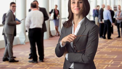 Eine Dame im schicken Kostüm, die in einem Foyer eines Messegebäudes steht und lächelt