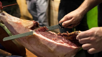 Ein Iberico-Schinken, von dem gerade eine hauchdünne Scheibe abgeschnitten wird