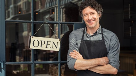 Gastronom steht lächelnd an der Tür, an der ein Open-Schild hängt